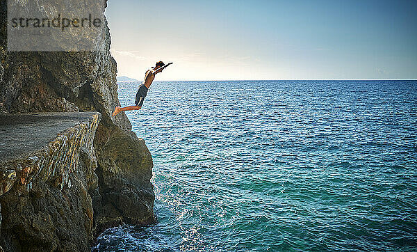 Junge springt von einer Klippe im Meer