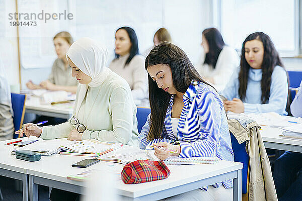 Multiethnische Freunde mit Büchern  die am Schreibtisch im Klassenzimmer lernen