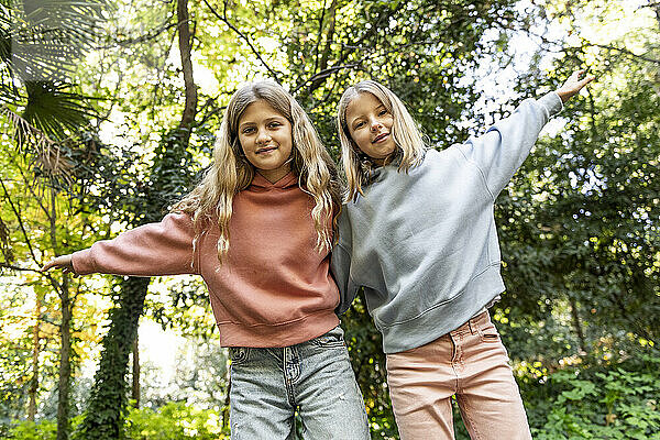 Smiling girls with arms raised standing in front of trees at park