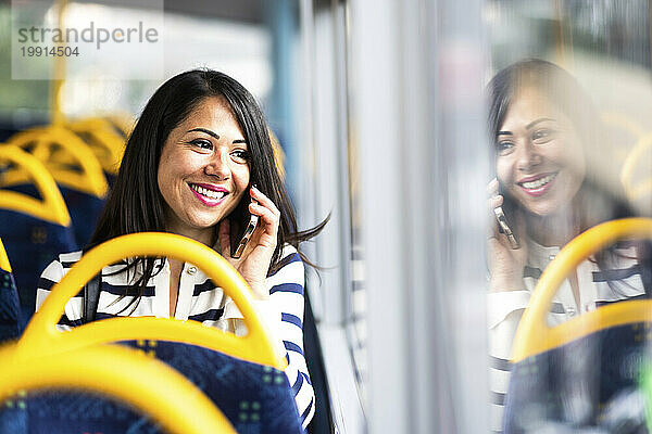 Glückliche Frau  die mit dem Smartphone spricht und im Bus reist