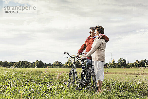 Liebevolles Seniorenpaar steht neben Fahrrad unter Himmel