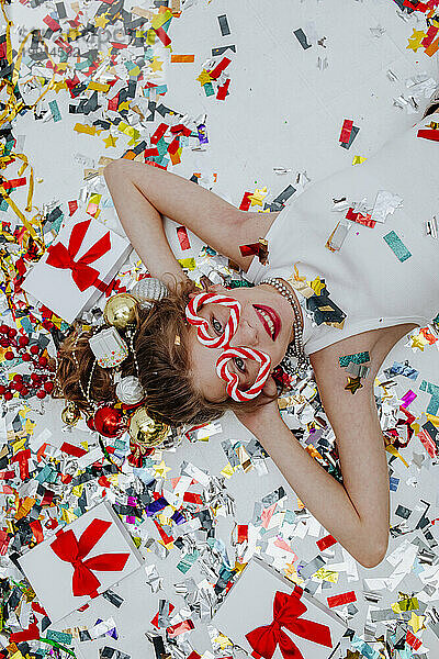 Lächelndes Mädchen liegt mit Konfetti neben Geschenkboxen auf weißem Boden