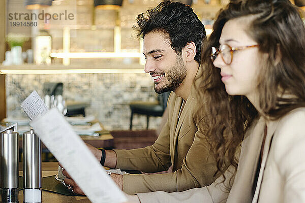 Lächelnde junge Kollegen lesen die Speisekarte im Restaurant