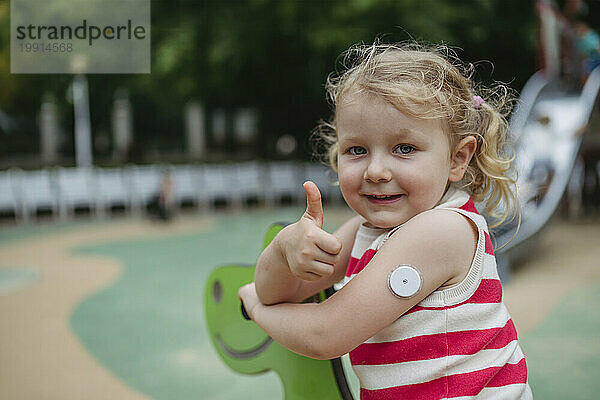 Little girl with diabetes giving thumbs up playing on seesaw on playground
