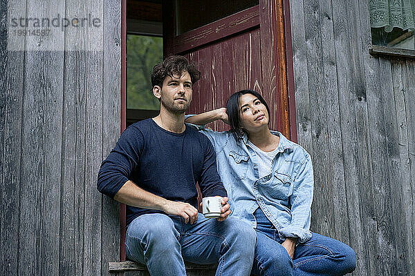 Junger Mann und Frau sitzen im Eingang einer Blockhütte