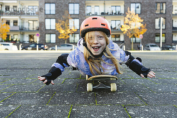 Glückliches Grundschulmädchen  das auf Skateboard liegt