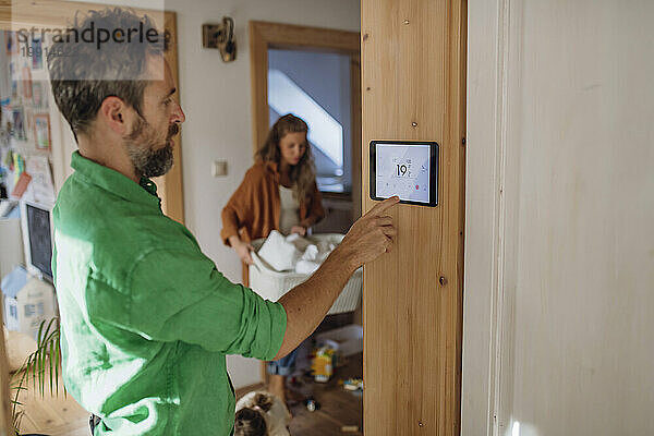 Mann regelt Temperatur über Hausautomations-App auf Tablet-PC  Frau im Hintergrund
