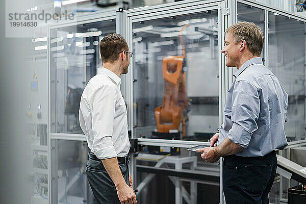 Zwei Geschäftsleute treffen sich am Industrieroboter in einer Fabrik