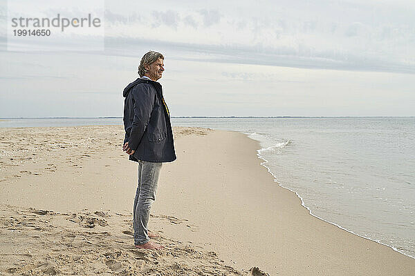 Älterer Mann steht am Strand am Meer
