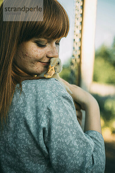 Young redhead woman with freckles holding duckling