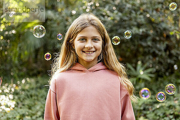 Happy blond girl with bubbles in park