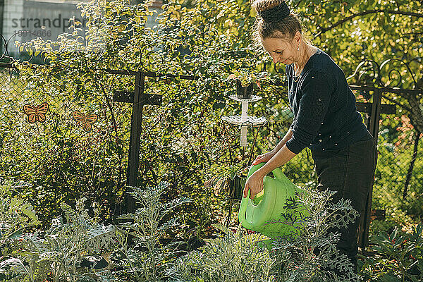 Lächelnde Frau  die Pflanzen im Garten gießt