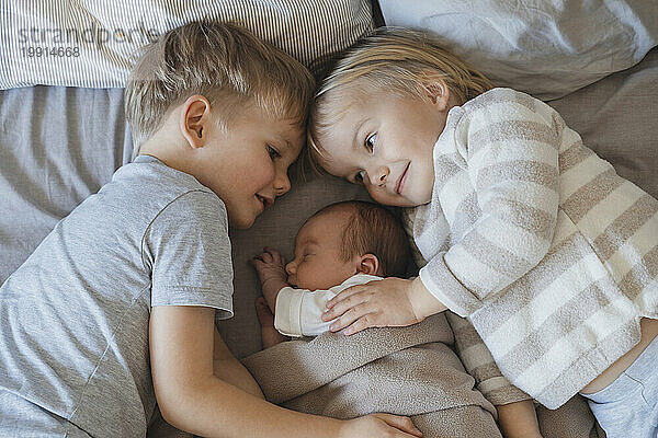Neugeborener Junge schläft neben Geschwistern  die im Bett liegen