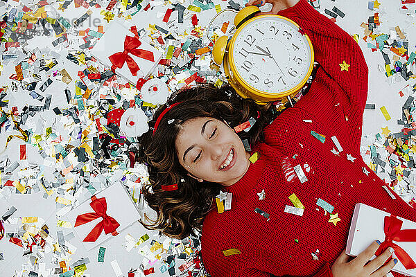 Happy girl lying on confetti with clock and gift boxes