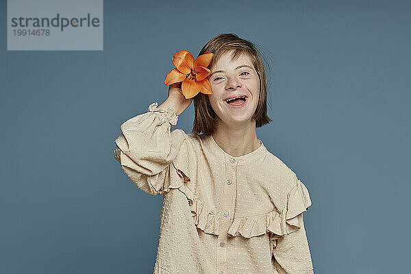 Cheerful teenage girl with Down syndrome with orchid flower against blue background