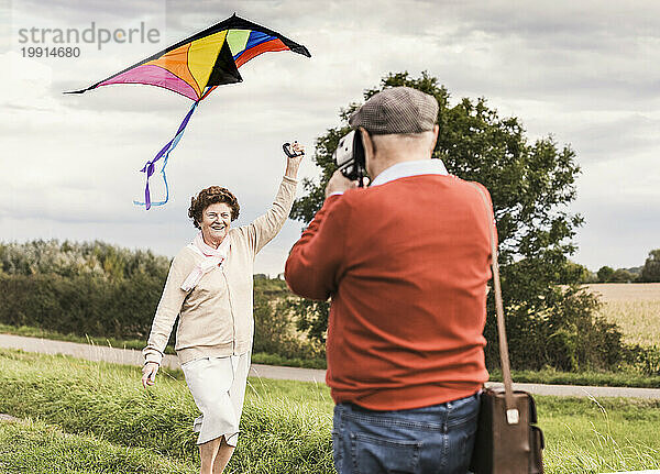 Älterer Mann fotografiert eine Frau  die auf dem Feld einen Drachen steigen lässt