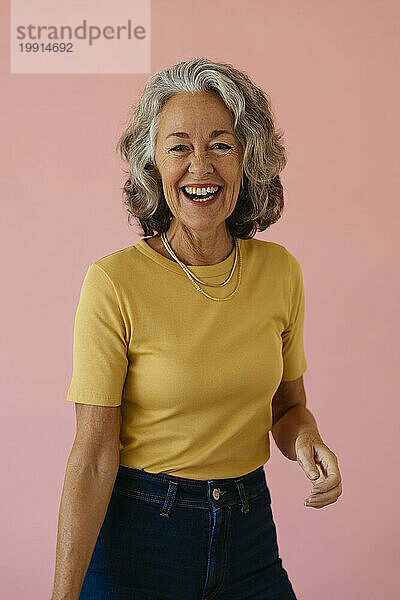 Glückliche ältere Frau  die vor rosa Hintergrund lacht