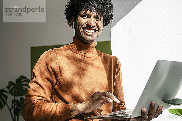 Lachender junger Freiberufler mit Laptop im Heimbüro