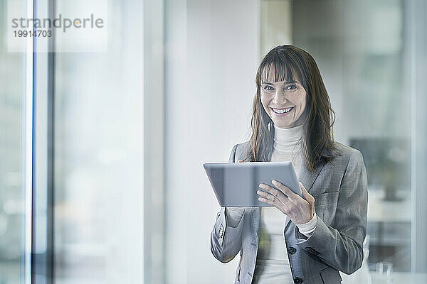 Glückliche reife Geschäftsfrau hält Tablet-PC durch Glas gesehen