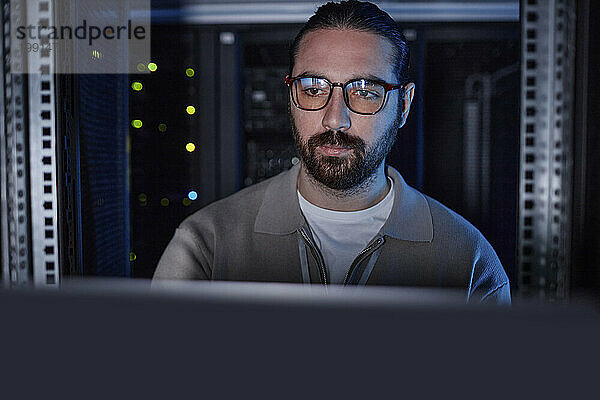 Junger Ingenieur trägt eine Brille und arbeitet am Laptop im Serverraum