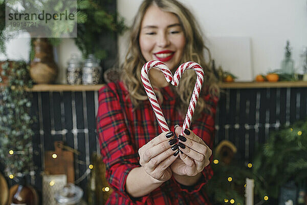 Smiling woman making heart shape with candy canes at home