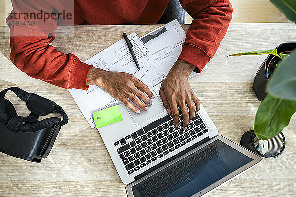 Freiberufler arbeitet am Laptop und prüft Dokumente am Schreibtisch im Heimbüro