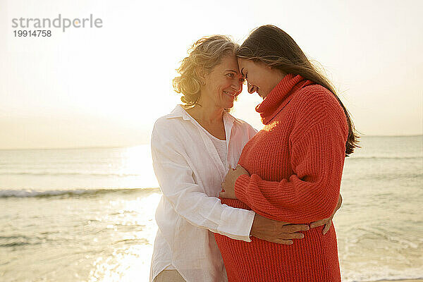 Glückliche Mutter und Tochter berühren einander am Strand die Stirn