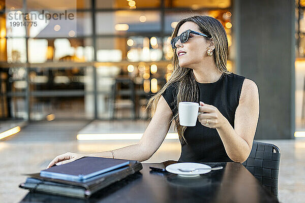 Geschäftsfrau mit Sonnenbrille und Kaffeetasse im Straßencafé