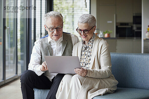 Älteres Paar sitzt zu Hause auf der Couch und nutzt Tablet-PC