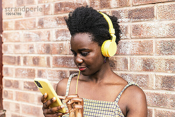 Junge Frau benutzt Smartphone und hört Musik vor einer Ziegelwand