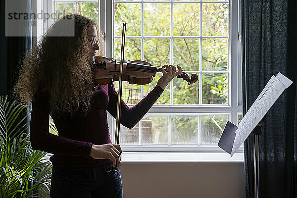 Mädchen spielt zu Hause vor dem Fenster Geige