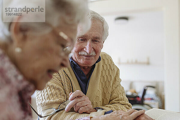 Smiling senior man with woman reading book and holding hands at home