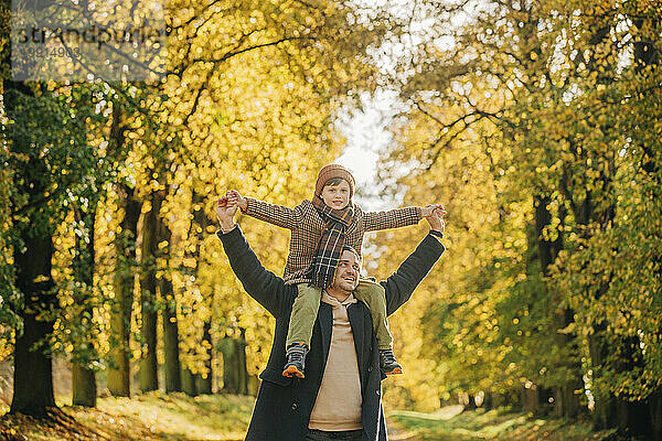 Glücklicher Vater trägt Sohn auf Schultern im Herbstpark