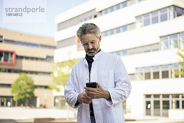 Arzt benutzt Mobiltelefon vor Gebäuden