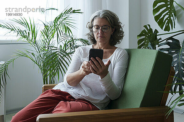 Frau mit Brille und smartem Sitzen auf einem Sessel zu Hause