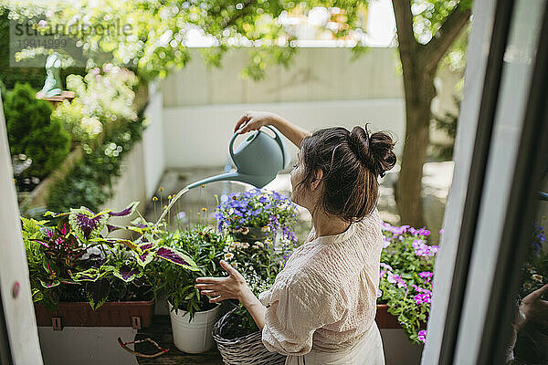 Woman watering flowers  taking care of plants on balcony