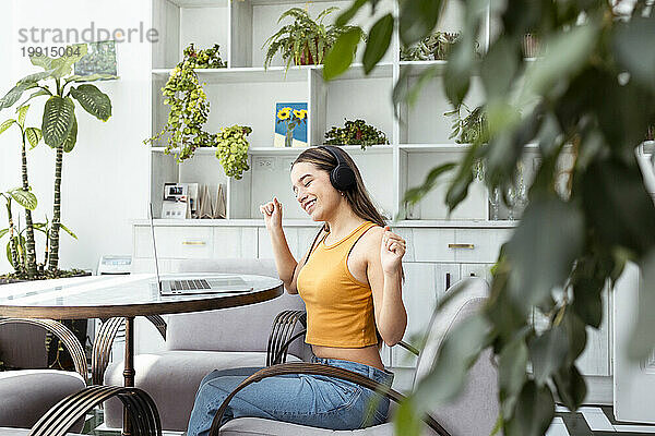 Frau mit geschlossenen Augen hört Musik und tanzt zu Hause in der Nähe eines Laptops