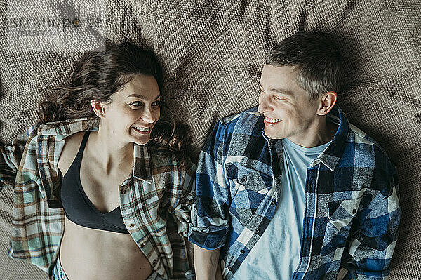 Smiling man and pregnant woman lying on bed at home