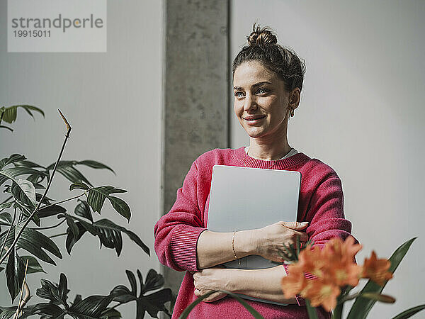 Lächelnde schöne Geschäftsfrau hält Laptop vor der Wand