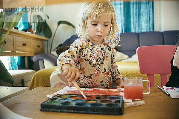 Mädchen malt zu Hause mit Pinsel und Aquarell auf Papier