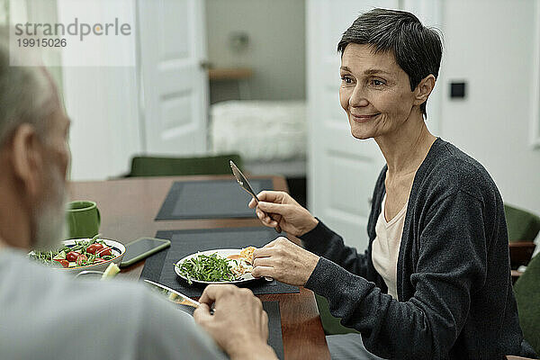 Erwachsene Frau schaut ihren Mann an  während sie Spiegeleier und Salat isst