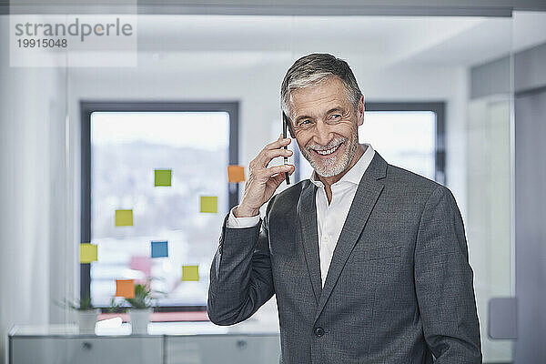 Glücklicher älterer Geschäftsmann  der im Büro auf dem Smartphone spricht