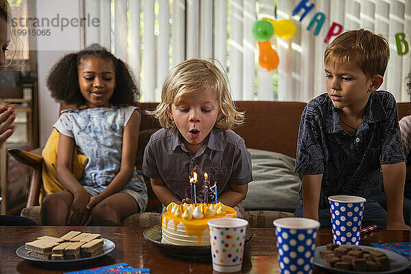 Junge bläst Kerzen auf seine Geburtstagstorte  während Freunde zuschauen