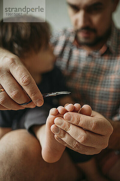 Vater schneidet zu Hause mit einer Schere die Zehennägel eines kleinen Jungen