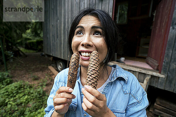 Happy woman holding pine cones in front of cabin