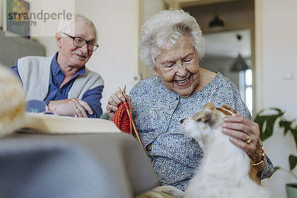 Happy senior woman stroking dog with man sitting at table