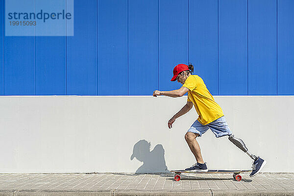 Junger Mann mit Behinderung fährt Skateboard in der Nähe einer Mauer