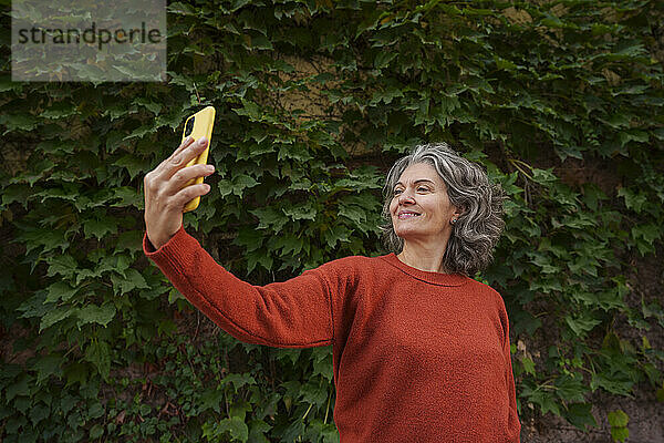 Lächelnde Frau  die vor Pflanzen ein Selfie mit ihrem Smartphone macht