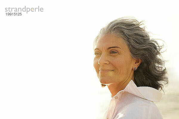 Lächelnde reife Frau mit grauen Haaren am Strand