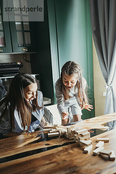Surprised mother and daughter looking at fallen blocks on table in kitchen